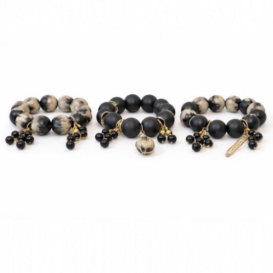 Handcrafted black and cream Afrocentric trio bracelet stack with 25mm painted beads, matte black beads and gold charm accents on white background