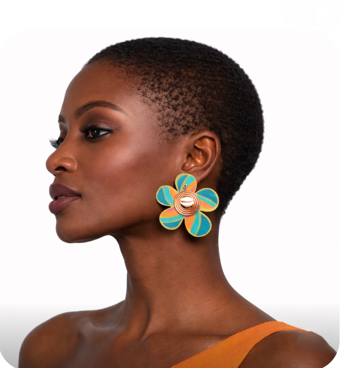 Alt Text:
Side profile of a beautiful dark skin woman with very short natural hair wearing colorful Afrocentric cowrie shell statement earrings on a clean white background