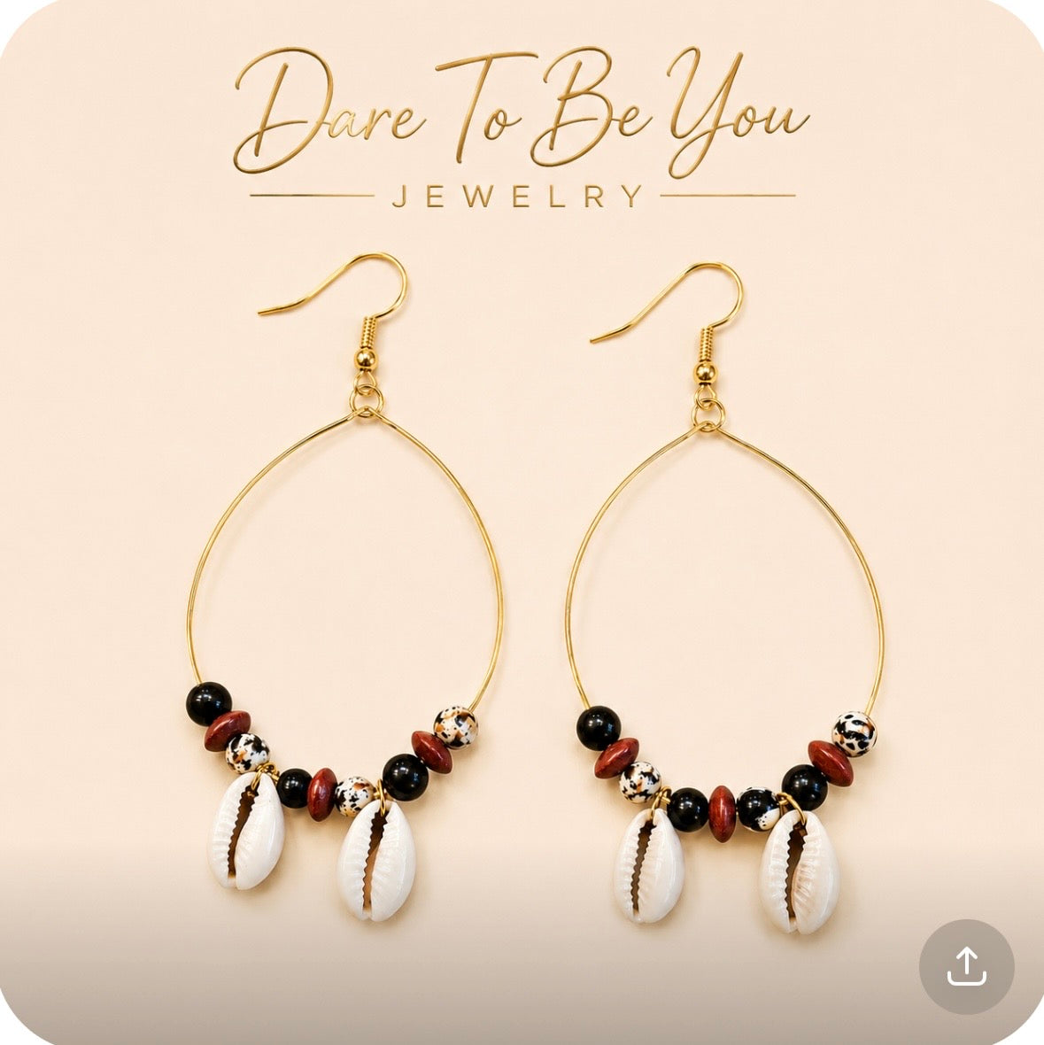 Afrocentric cowrie shell gold wire hoop earrings with black beads, speckled beads, and wood accents on a cream background by Dare To Be You Jewelry.