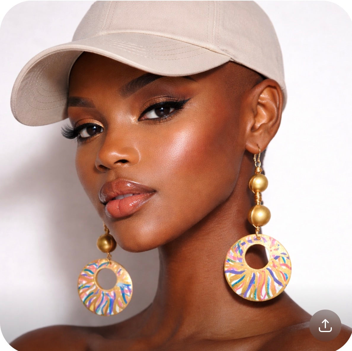 Dark skin bald woman wearing baseball cap and Afrocentric golden radiance color splash statement earrings front view