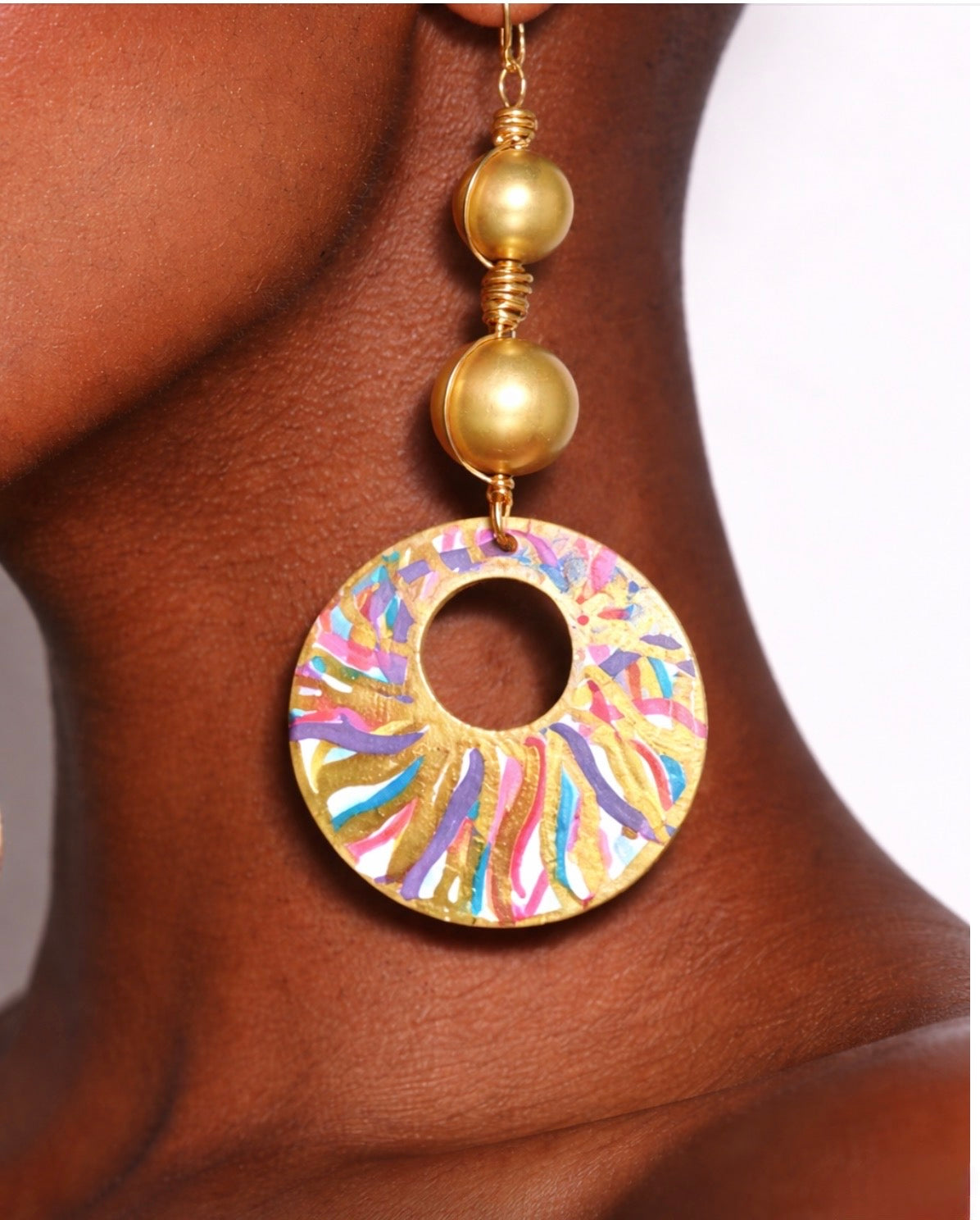 Close up of Afrocentric golden radiance color splash statement earrings on dark skin model showing detailed hand painted design