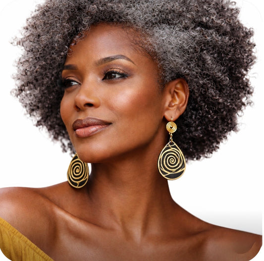 Dark skin middle-aged woman with grey afro wearing medium-sized Afrocentric black and gold spiral statement earrings on clean white background, facing forward confidently