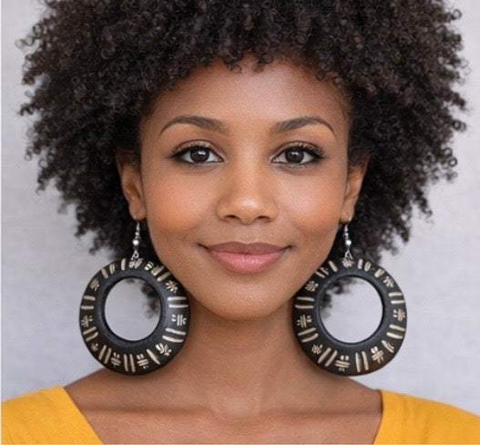 Brown skin woman with afro wearing Afrocentric black hoop earrings facing forward in mustard yellow top