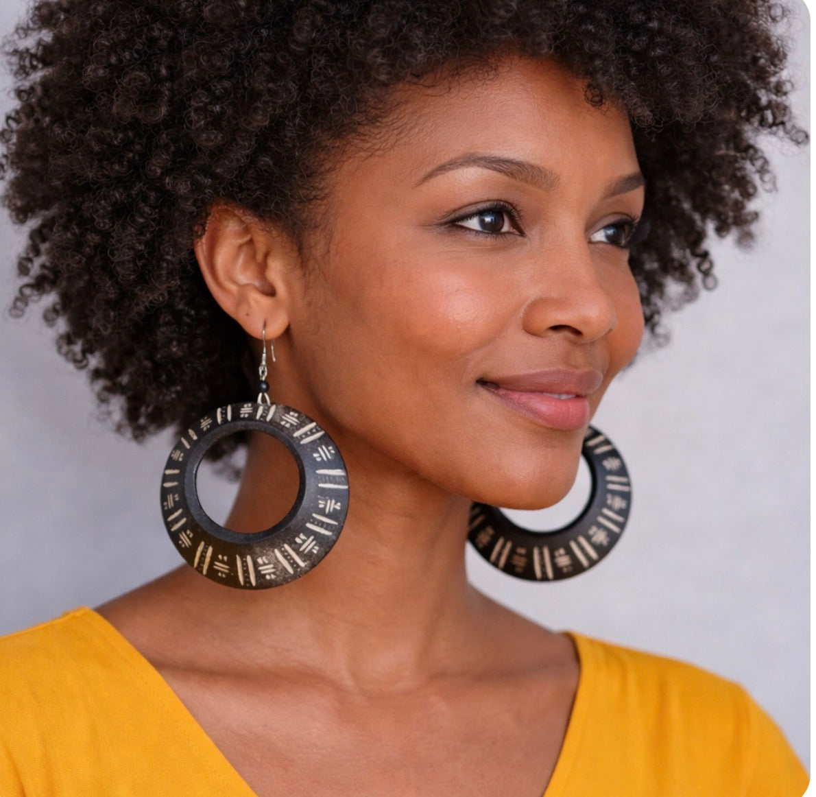 Brown skin woman wearing Afrocentric black hoop earrings in mustard yellow top side view