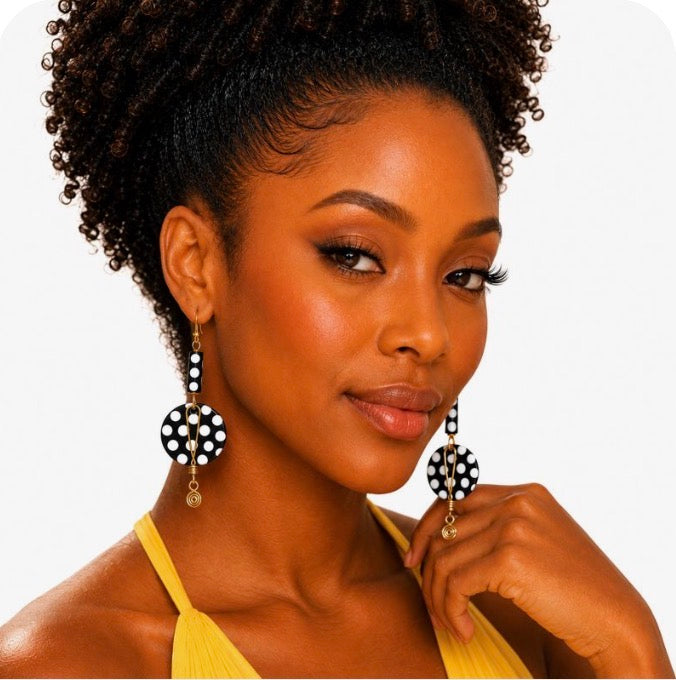 Close-up portrait of a sophisticated Black woman wearing handmade Afrocentric black and white polka statement earrings with gold accents by Dare To Be You Jewelry on a clean white background.