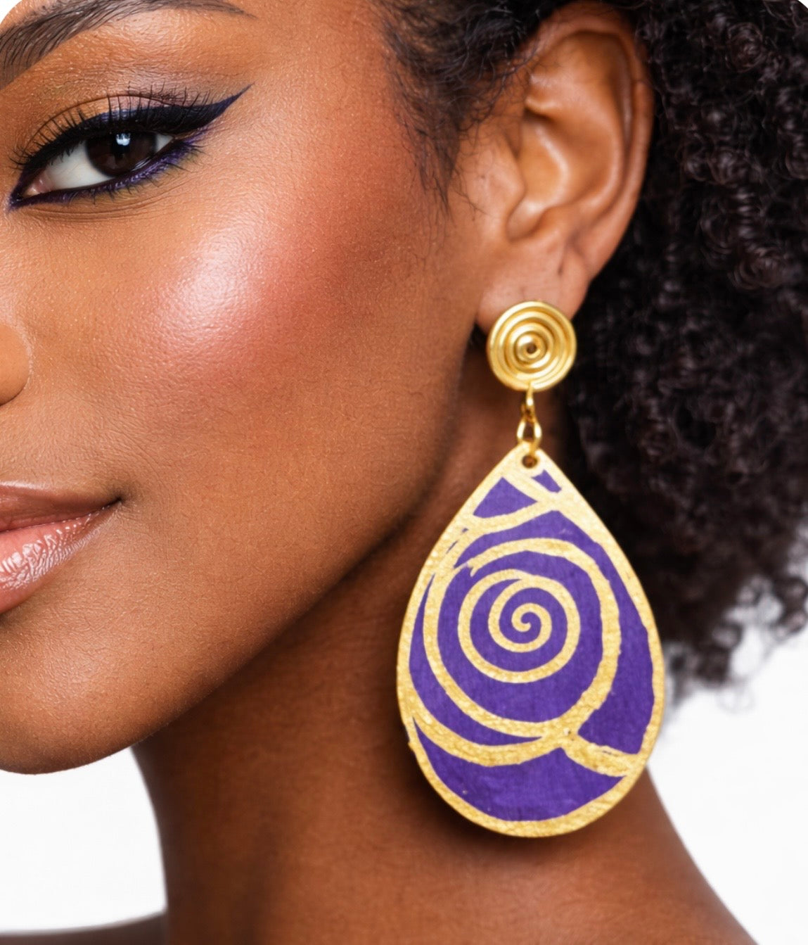 Close-up of dark skin woman wearing purple and gold Afrocentric statement earrings showing detailed spiral design and handcrafted texture