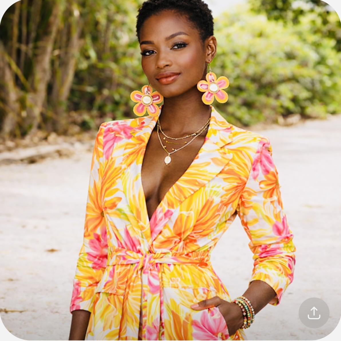 Dark skin woman with short natural hair wearing Afrocentric Sunset Bloom Earrings and a vibrant floral pantsuit in an outdoor lifestyle photo