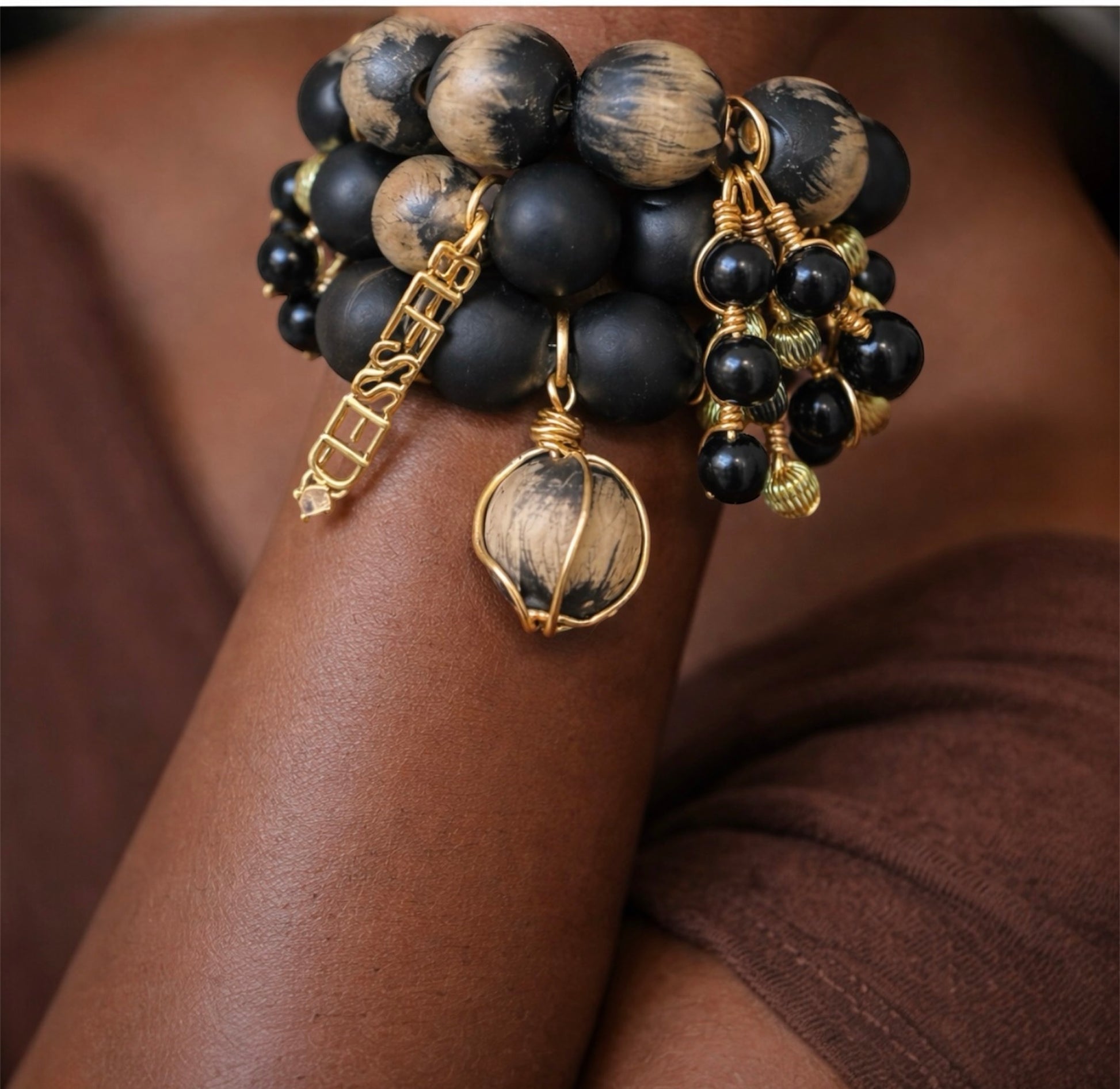 Close-up of handcrafted black and cream Afrocentric bracelet stack with 25mm painted beads and gold charms on brown skin wrist