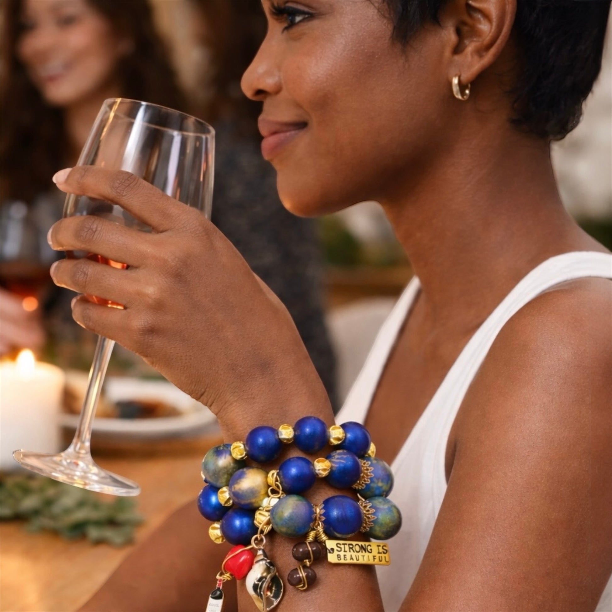 Brown skin woman wearing bold 25mm hand-painted wood bead bracelet trio in blue and gold at social gathering showing confident Afrocentric style