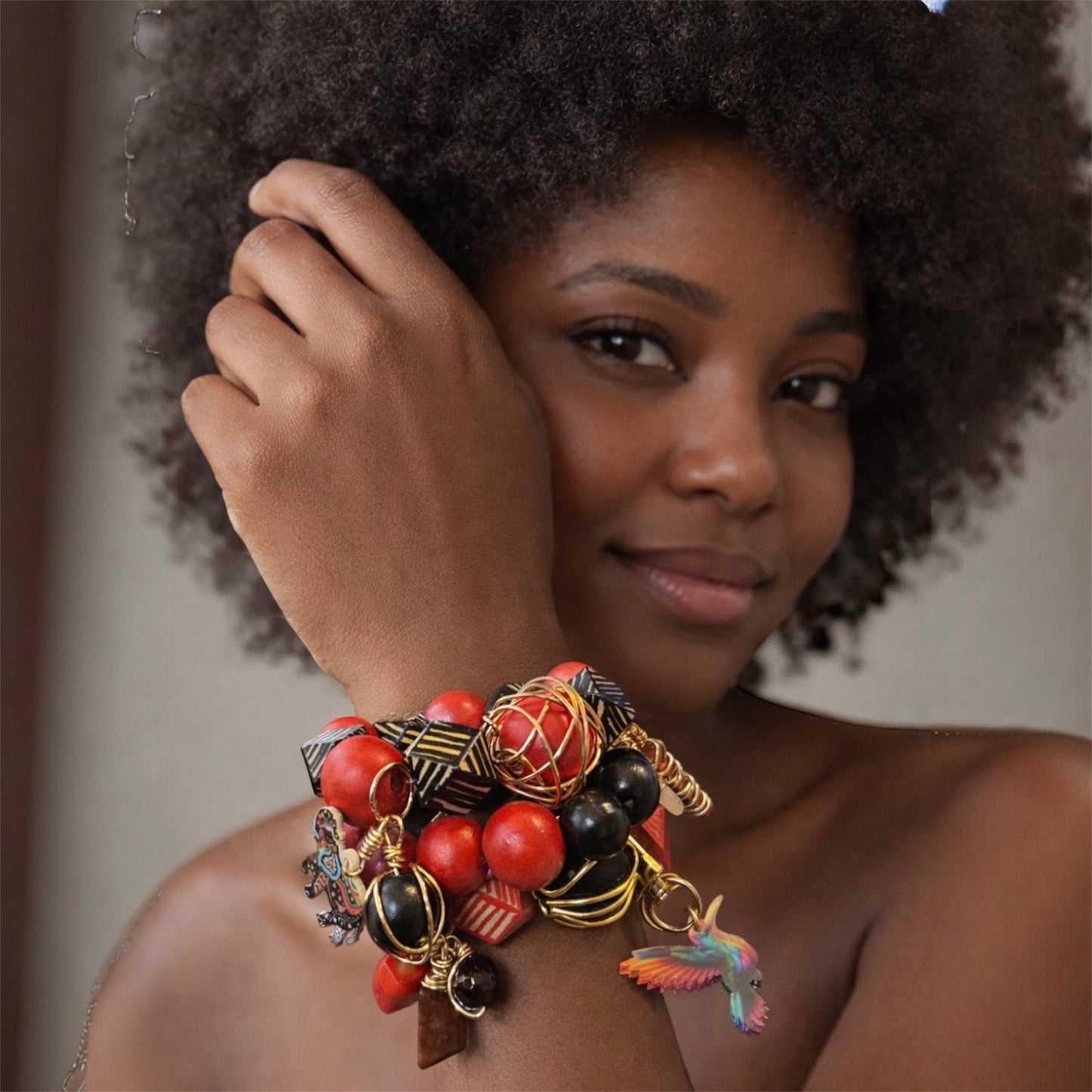 handmade Afrocentric chunky stack with red and black wooden beads, goldwire accents, geometric beads and colorful hummingbird charm on white background 