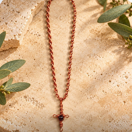 Earthbound Spirit handmade pure copper necklace featuring a wire-wrapped cross pendant with black glass bead and handcrafted copper link chain on a warm earthy background with greenery.