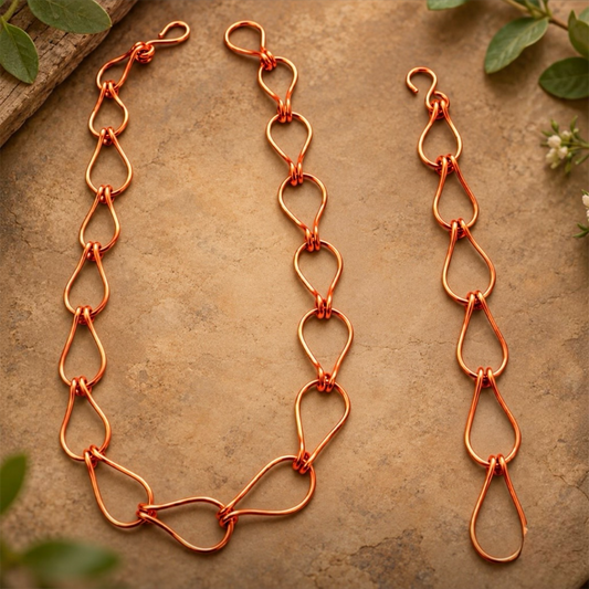 Ember Drop Handmade Copper Link Necklace and Bracelet Set featuring handcrafted teardrop-shaped pure copper wire links with a warm, polished shine, beautifully displayed on an earthy stone background with natural greenery.