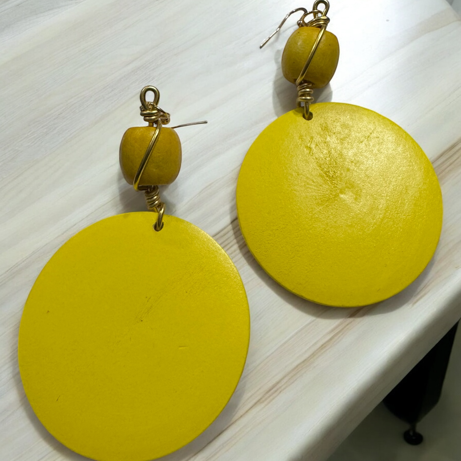 Close-up view of handmade yellow wood earrings with gold wire wrap.