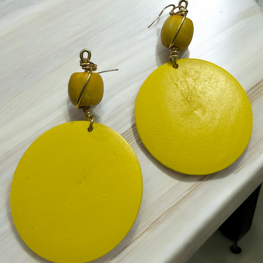 Close-up view of handmade yellow wood earrings with gold wire wrap.