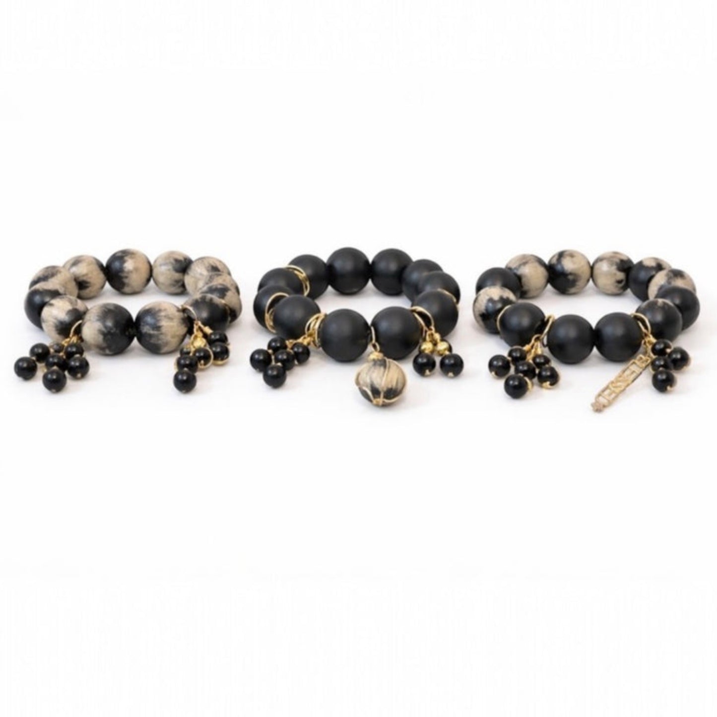 Handcrafted black and cream Afrocentric trio bracelet stack with 25mm painted beads, matte black beads and gold charm accents on white background